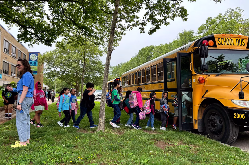 Children line up to board a yellow school bus, while an adult looks on. They